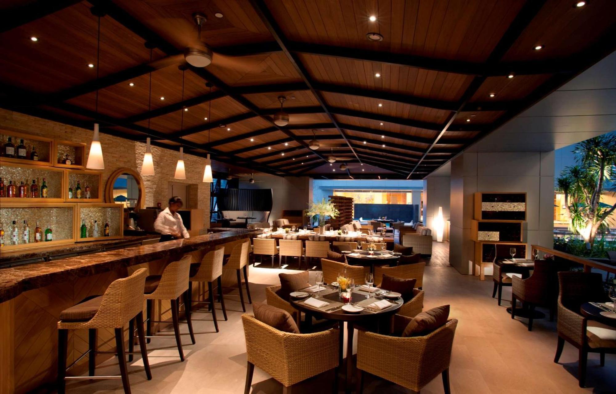 Doubletree By Hilton Kuala Lumpur Hotel Exterior photo The photo shows an upscale restaurant interior with a warm and inviting ambiance. There is a large wooden bar area on one side, with bar stools arranged around it. The ceiling features wooden beams and modern lighting fixtures, creating a cozy atmosp