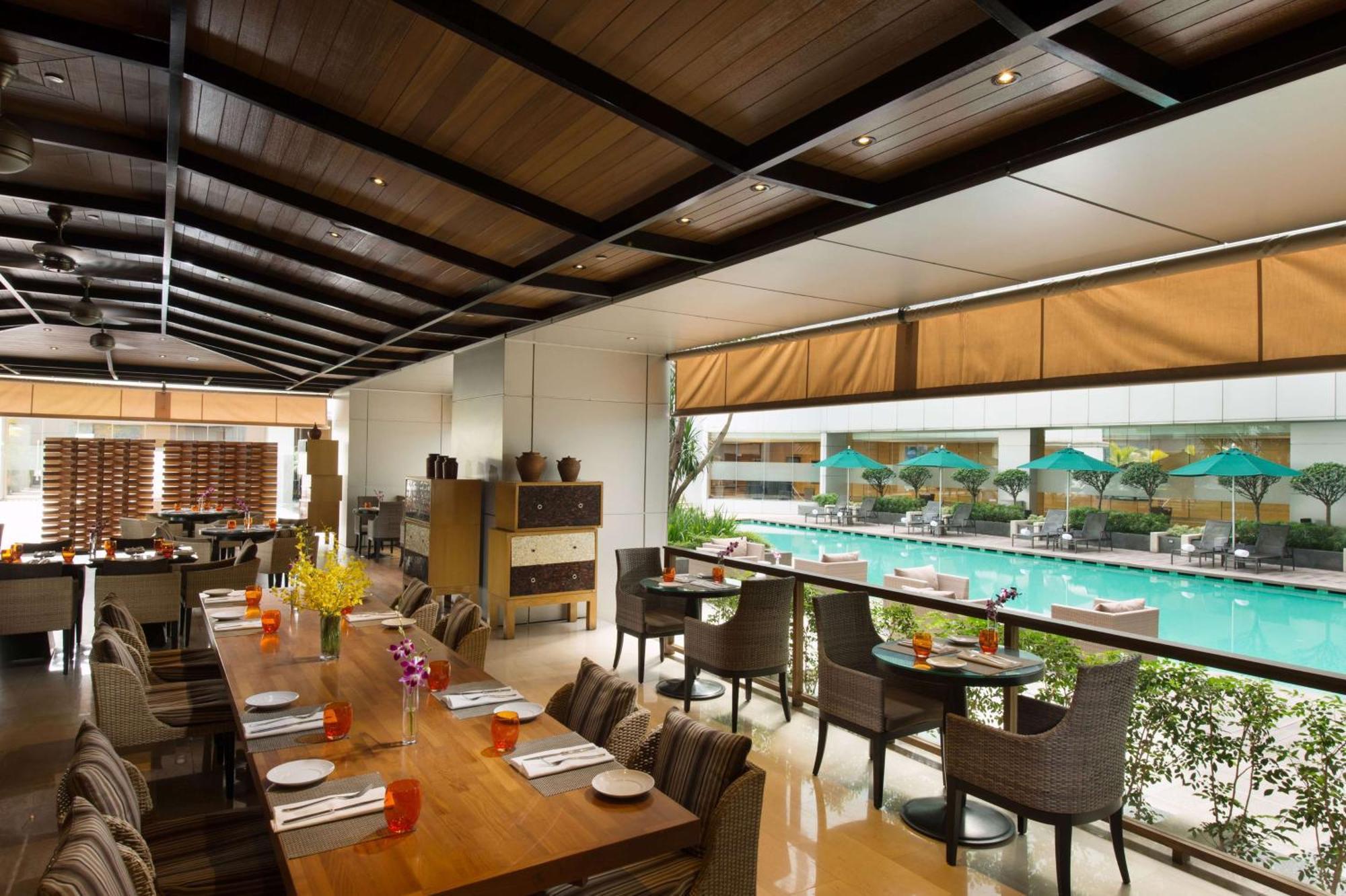 Doubletree By Hilton Kuala Lumpur Hotel Exterior photo The photo shows an indoor restaurant area with a modern and stylish design. There are several tables set for dining, featuring place settings and drinks. Large windows allow for a view of a swimming pool outside, which is adorned with umbrellas. The 